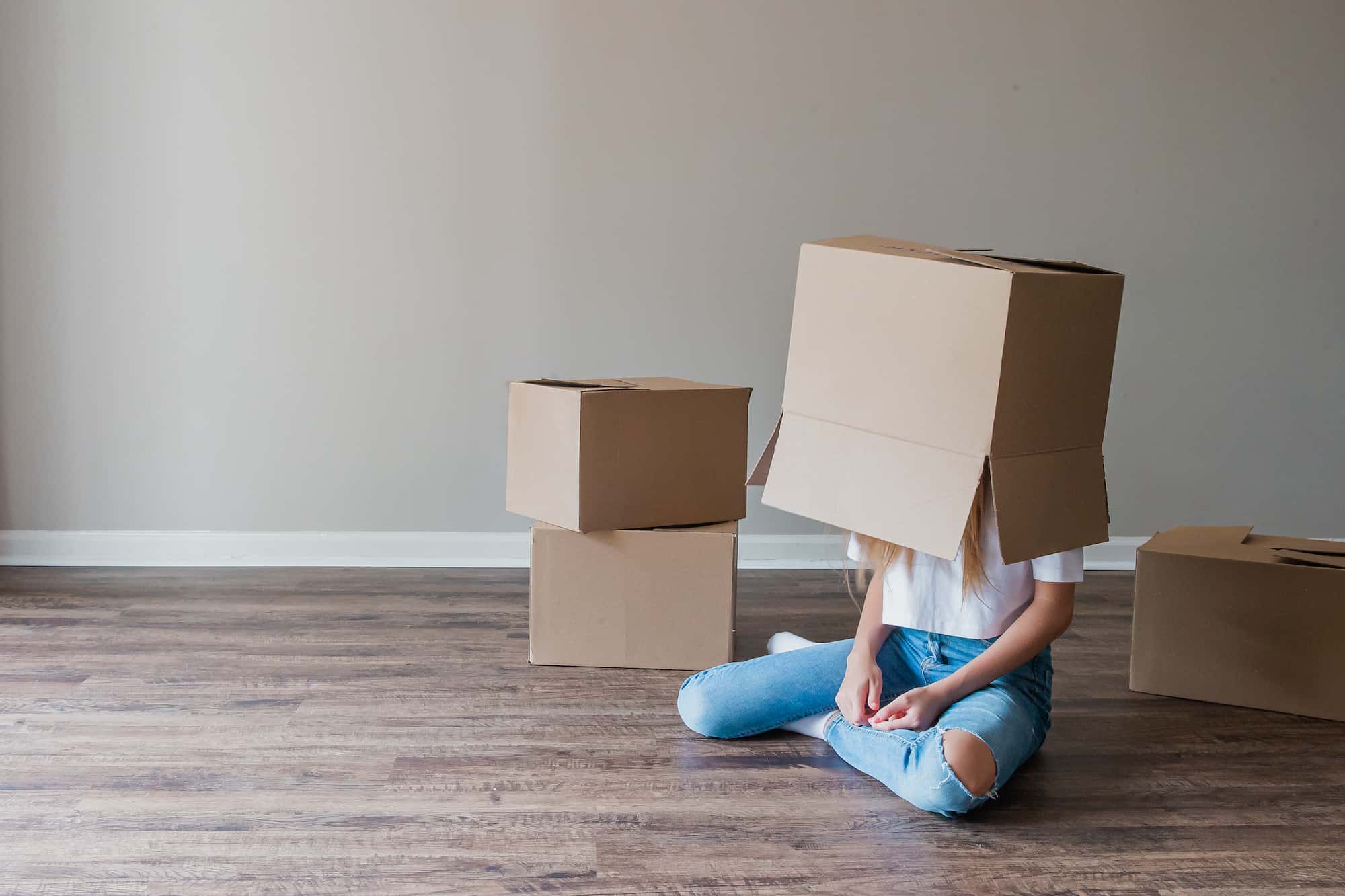 Una joven feliz cargando una caja de cartón mientras se muda a su nueva casa, representando la necesidad de trasteros para estudiantes en verano